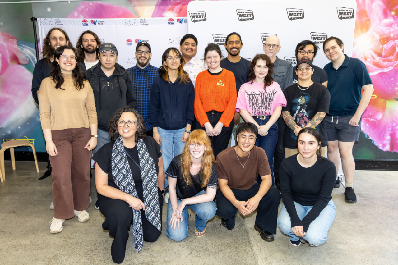 Group of 20 people standing in front of a media wall smiling